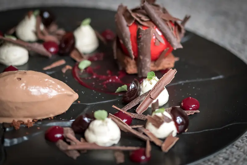 Black Forest dessert plate with chocolate mousse, cherries, whipped cream rosettes, chocolate shavings, and berry coulis