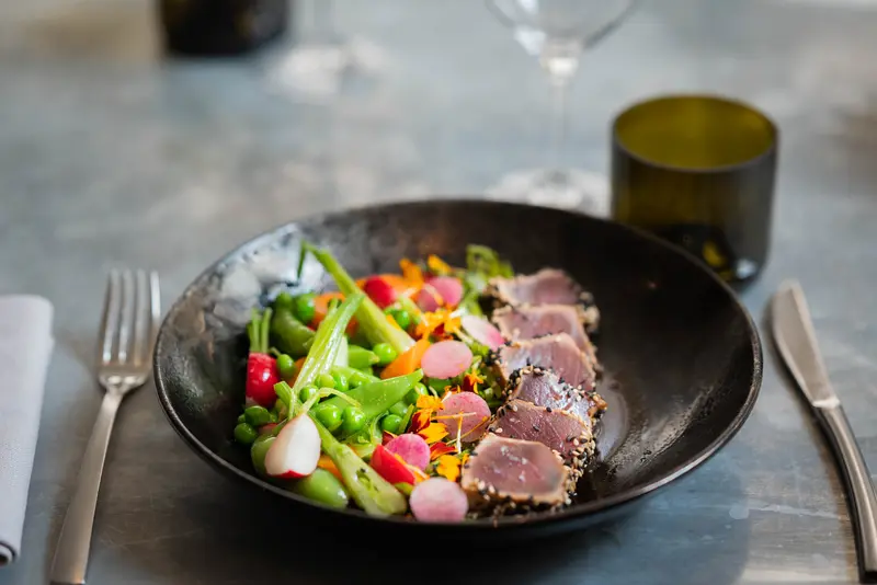 Seared sesame-crusted tuna with spring peas, radish, snap peas, and edible flowers in a black bowl