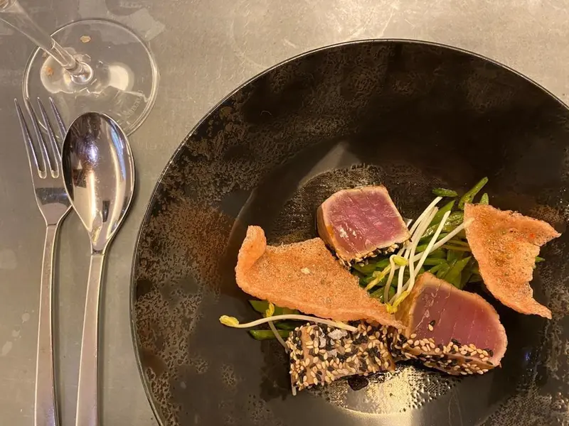 Seared sesame-crusted tuna with microgreens and crispy rice crackers on a black ceramic plate at a fine dining restaurant.