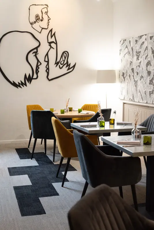 Elegant restaurant dining room with velvet chairs, artistic wall mural, green glassware, and geometric carpet in modern setting.