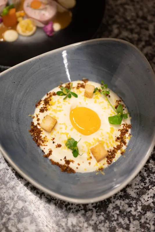 Elegant creamy soup with egg yolk, croutons, microgreens, and breadcrumbs in a blue ceramic bowl at fine dining restaurant