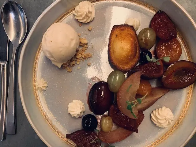 Roasted stone fruits with vanilla ice cream, cream rosettes, and candied grapes on artisan ceramic plate