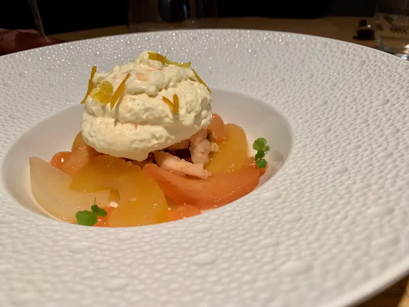 Elegant dessert with poached peaches, whipped cream, and candied citrus zest in a white textured bowl