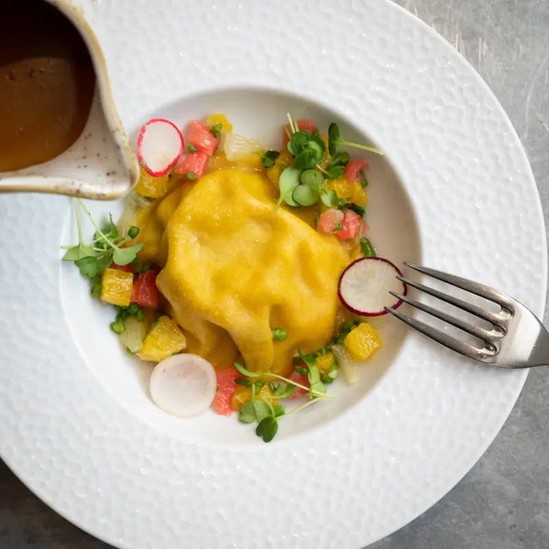 Yellow pasta dumpling with citrus salad, radish, microgreens, and brown butter sauce at upscale restaurant
