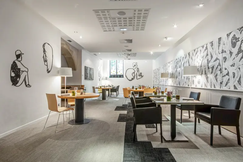 Modern restaurant dining room with black leather chairs, artwork murals, warm lighting, and elegantly set tables.