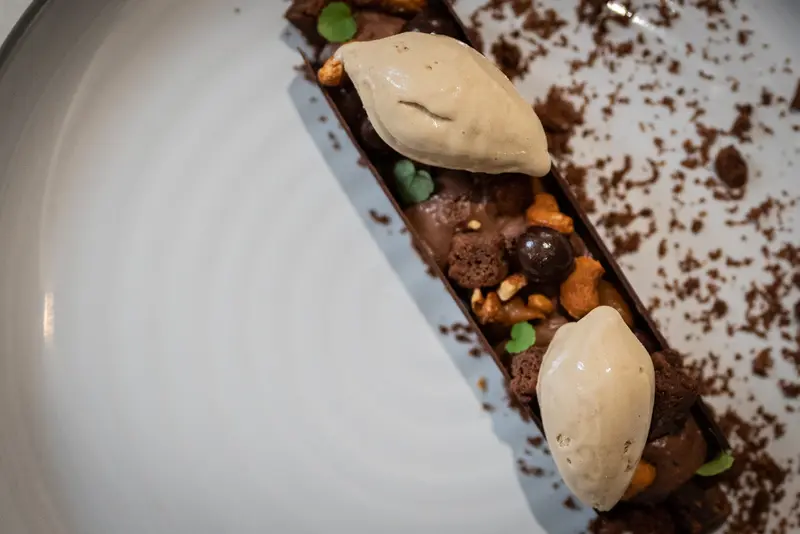 Elegant chocolate dessert tart with caramel mousse quenelles, candied nuts, and cocoa crumble on a white plate.