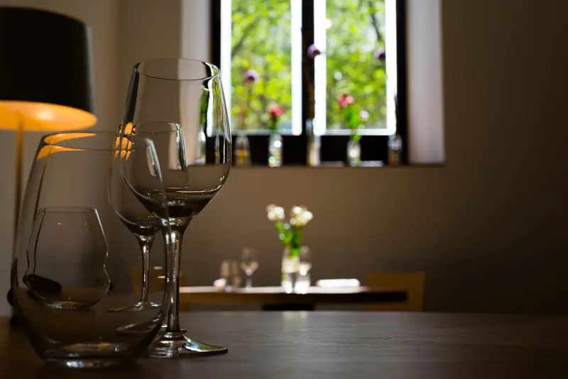 Elegant restaurant interior with empty wine glasses on dark wood table, warm lighting, and garden view window.