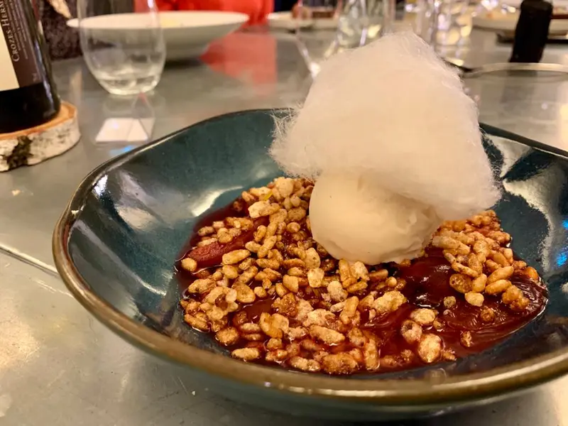 Elegant dessert bowl with puffed rice, fruit compote, vanilla ice cream, and cotton candy at a fine dining restaurant.