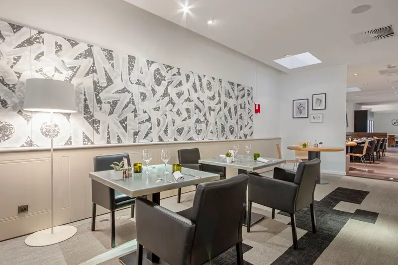 Modern restaurant dining room with leather chairs, set tables, wine glasses, and large abstract wall art mural.