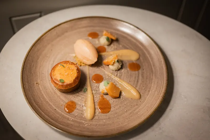 Elegant plated dessert with sorbet, caramel sauce dots, cream quenelles, and a golden tart on rustic ceramic plate.