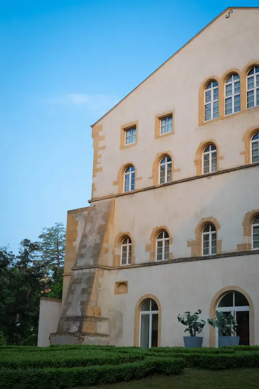 Historic French château exterior with arched windows, manicured hedges, and potted plants — elegant restaurant venue setting.