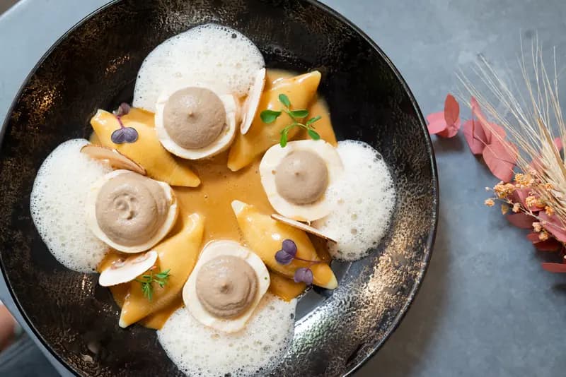 Elegant scallops with mushroom mousse, mango coulis, foam, and microgreens in a dark bowl — fine dining presentation