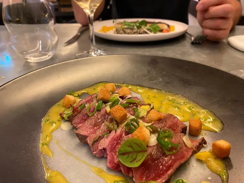Sliced medium-rare steak with yellow sauce, croutons, and scallions on a dark plate at an upscale restaurant dinner.