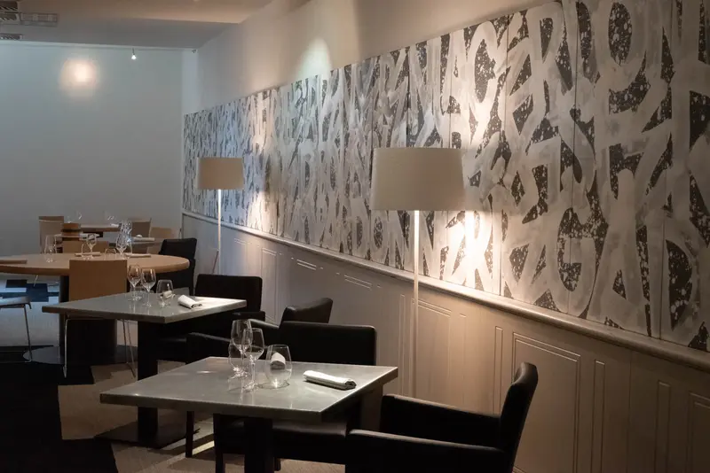 Elegant restaurant dining room with black chairs, set tables, wine glasses, and abstract black-and-white wall art panels