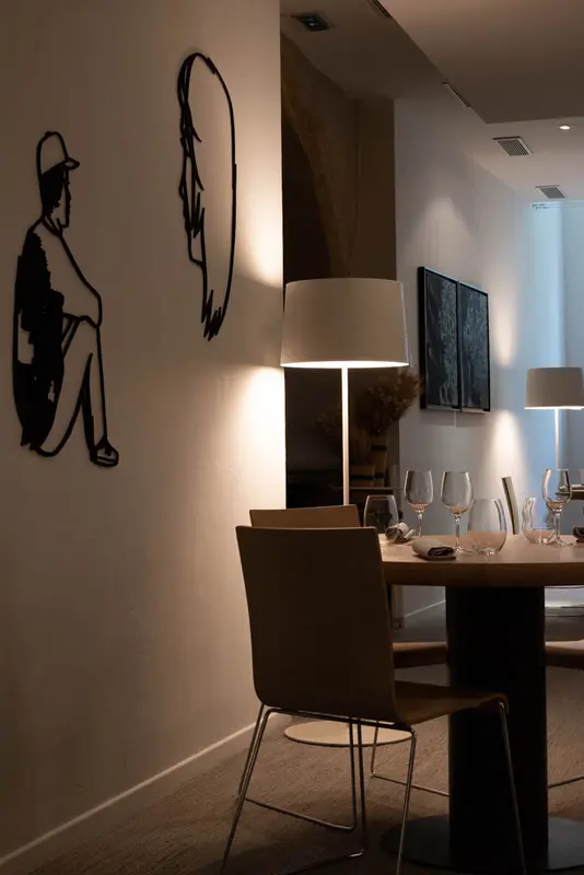 Elegant restaurant dining room with warm lighting, set wine glasses, wooden chairs, and modern wall art silhouettes