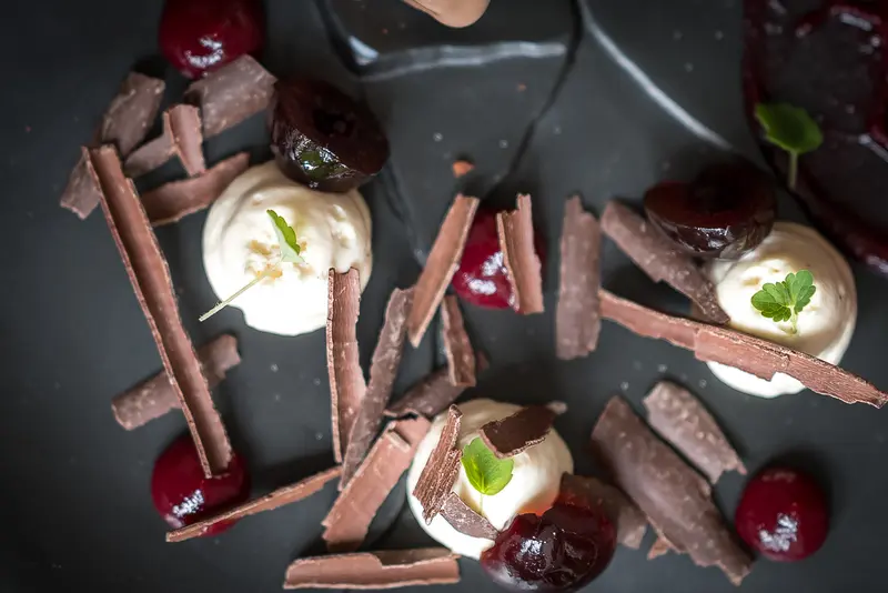 Elegant chocolate shavings dessert with cherries, whipped cream, and fresh mint on a dark slate plate